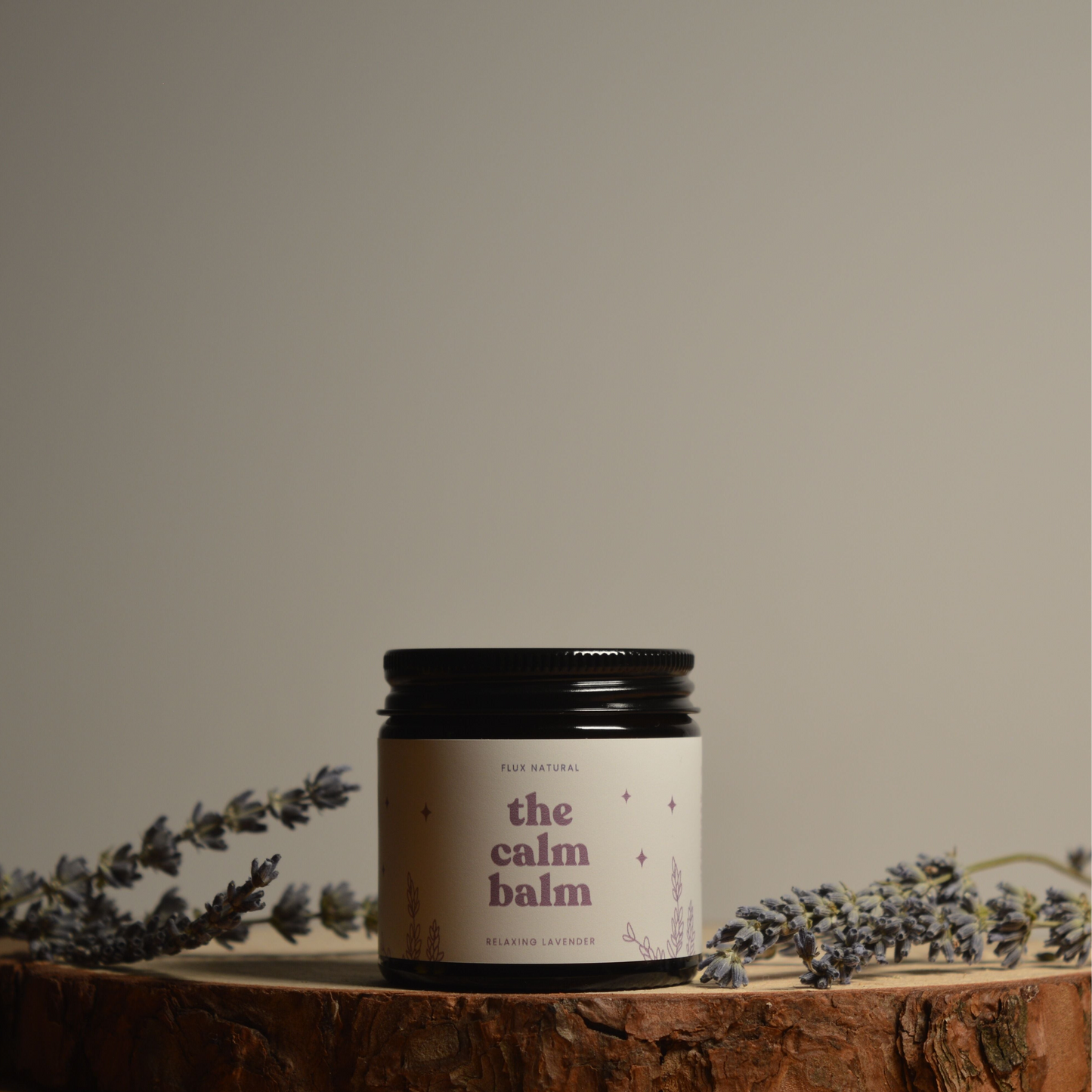 Jar of 'the calm balm' surrounded by lavender on a wooden surface with a neutral background