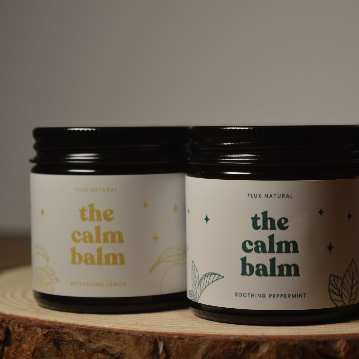 Three jars of 'the calm balm' on a wooden surface with a dark background