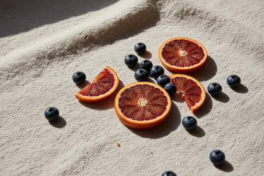 Sliced blood orange with scattered blueberries on textured neutral surface in natural light