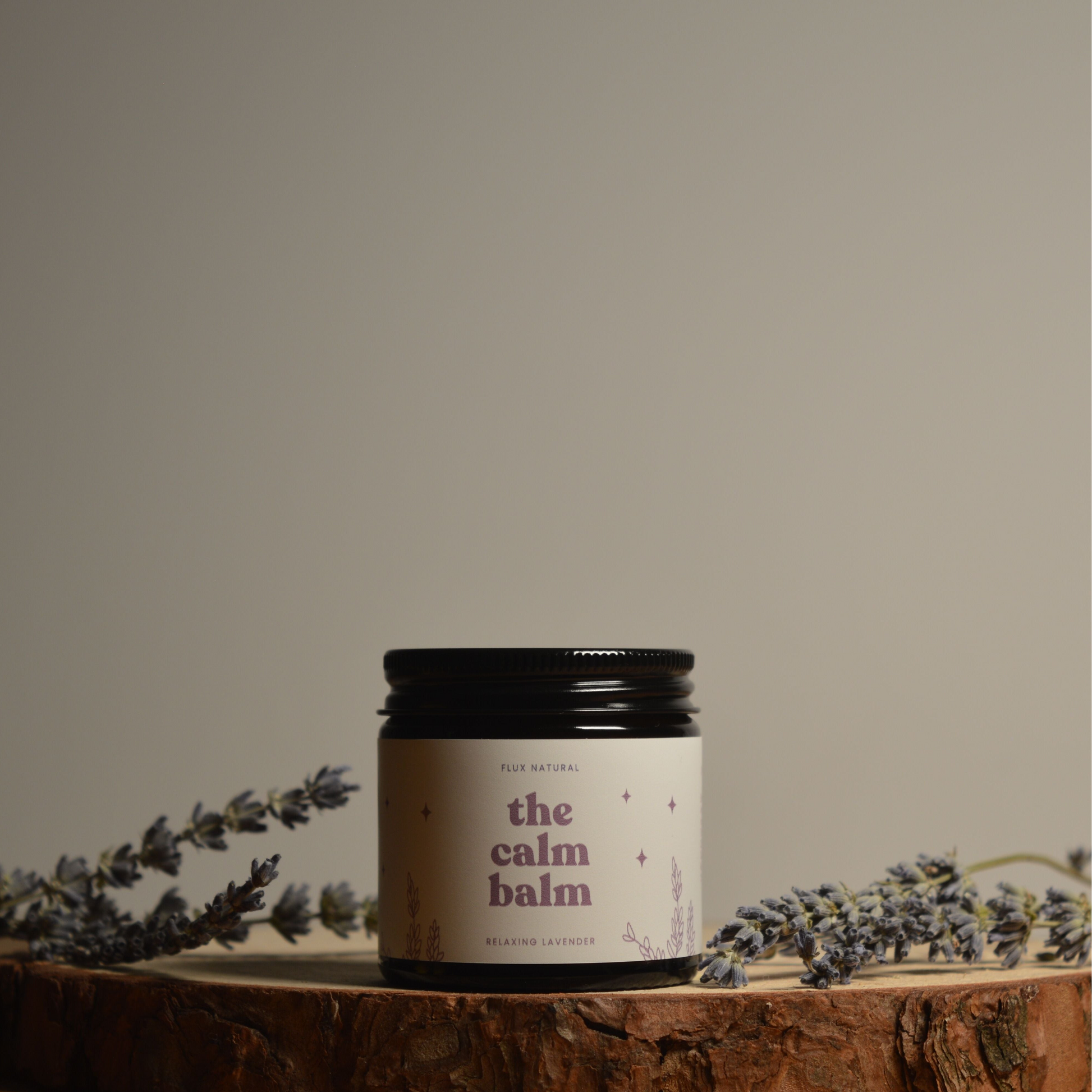 Jar of 'the calm balm' surrounded by lavender on a wooden surface with a neutral background